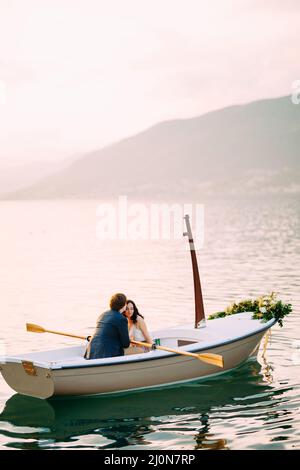 L'homme embrasse la femme sur le front dans un bateau décoré de fleurs au milieu d'un étang sur un fond de montagnes Banque D'Images