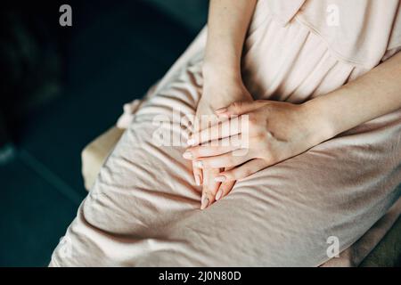 Femme vêtue d'une robe beige, elle a plié les mains sur ses genoux, assise sur une chaise.Gros plan Banque D'Images