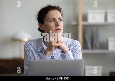 Inquiet femme d'affaires frustrée et mûre assise sur un ordinateur portable au bureau Banque D'Images