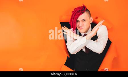 Un jeune homme sérieux avec des dreadlocks rouges montre un geste de fin d'arrêt par des mains croisées croisant les mains, avertissement gestuel ou interdiction, à travers un trou dans le TH Banque D'Images