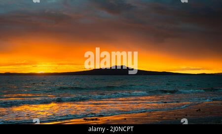 Soleil levant sur l'île Rangitoto, Milford Beach, Auckland. Banque D'Images