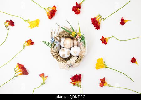 Nicher avec des œufs blancs et dorés, avec des fleurs jaunes et rouges sur fond blanc. Pâques. Copier l'espace Banque D'Images