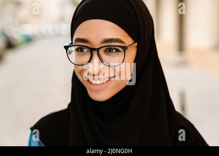 Gros plan d'une jeune musulmane souriante dans un hijab debout dans une rue Banque D'Images