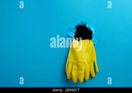 Une paire de gants de nettoyage en latex jaune qui dépassent du trou déchiré du fond en papier bleu Banque D'Images