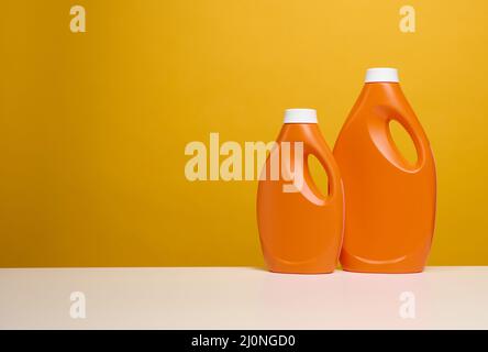 Deux flacons en plastique orange avec détergent liquide sont sur une table blanche, sur fond jaune Banque D'Images