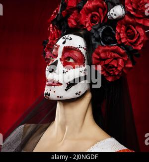 Portrait d'une belle femme avec un maquillage de crâne de sucre avec une couronne de fleurs sur sa tête, fond rouge Banque D'Images