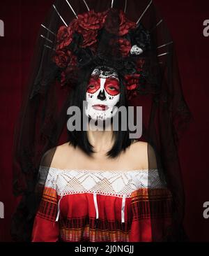 Portrait d'une belle femme avec un maquillage de crâne de sucre avec une couronne de fleurs sur sa tête, fond rouge Banque D'Images