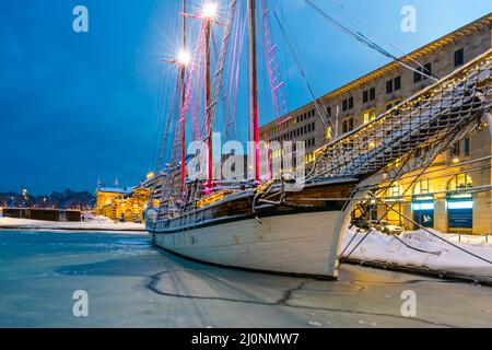 Un voilier en bois amarré au port pendant une nuit hivernale glacielle. Bateau historique au milieu de l'eau gelée couverte de floe dans les belles lumières. Banque D'Images