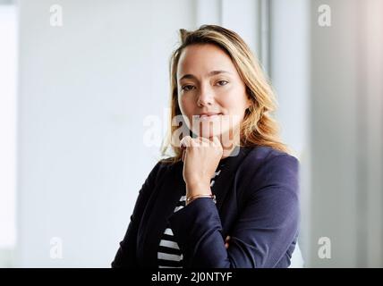 Shes auto-fabriqué et indépendant. Portrait d'une femme d'affaires attirante posant avec sa main sur son menton au travail. Banque D'Images