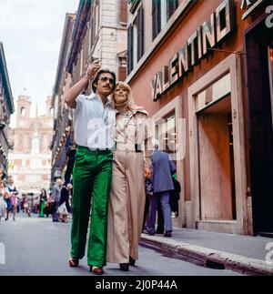 Vintage Rome 1970s, couple élégant se promener par le magasin de mode Valentino, rue commerçante via dei Condotti, Italie, Europe, Banque D'Images