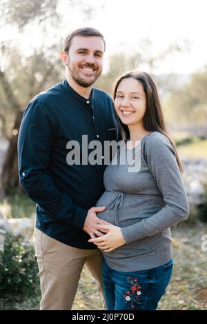 Homme souriant tenant les mains sur le ventre de la femme enceinte Banque D'Images