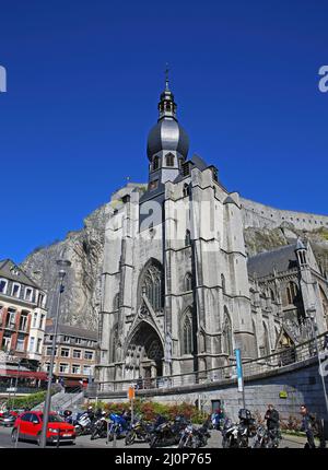 Dinant, Belgique - Mars 9. 2022: Vue à angle bas sur l'église gothique médiévale contre la face rocheuse abrupte avec la citadelle, ciel bleu d'hiver clair sans nuages Banque D'Images