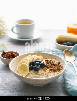 Flocons d'avoine entiers, grand bol de porridge avec banane, baies, noix pour le petit déjeuner. Vue latérale, verticale Banque D'Images