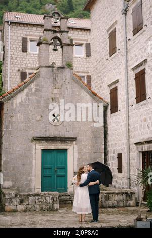 Marié embrasse la mariée près de la porte verte de l'ancienne église.Vue arrière Banque D'Images