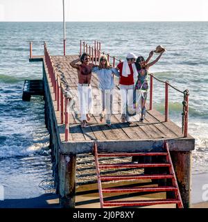 Vintage Italie 1970s, exubérant 2 couples de joyeux amis courant sur la jetée, plage Kursaal, Lido di Ostia, Lazio, Europe, Banque D'Images