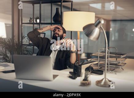 La nuit a été beaucoup plus longue. Photo d'un jeune homme d'affaires se sentant stressé en travaillant tard dans la nuit dans un bureau moderne. Banque D'Images