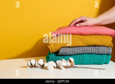 Femme tenant une pile de chandails tricotés pliés sur un fond jaune. Laver les vêtements, nettoyer les choses Banque D'Images