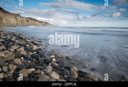 Plage tropicale de galets vide sous des falaises avec des vagues de vent et ciel nuageux Banque D'Images