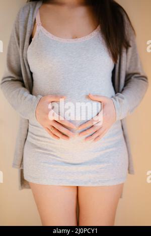 La femme enceinte se tient près du mur en tenant ses mains sur son ventre Banque D'Images