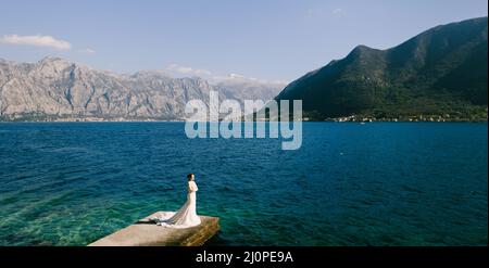 Mariée dans une longue robe se tient sur un quai au milieu de la baie, entouré de montagnes.Vue de dessus Banque D'Images