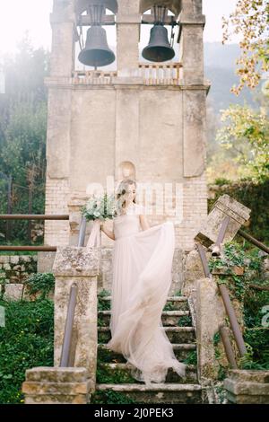 La mariée avec un bouquet se dresse sur un escalier en pierre devant une ancienne chapelle Banque D'Images