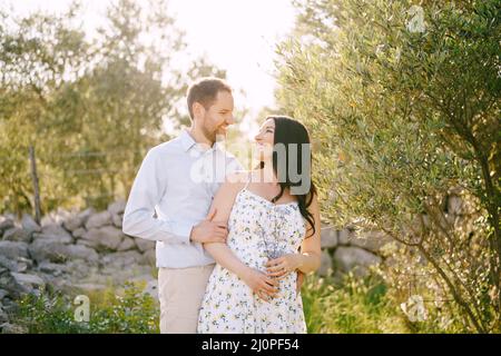 Homme embrassant de derrière une femme enceinte tenant des fleurs sauvages Banque D'Images