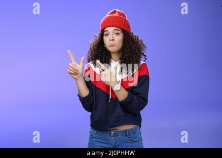 Portrait de la femme richement bouleversée mignonne cully-cheveux dans le beanie à la mode qui puise les lèvres dans la tristesse et frowning faisant déçu, regre Banque D'Images