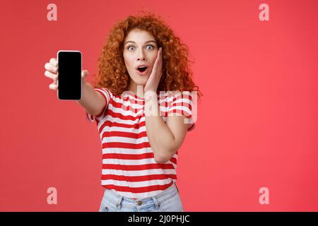 Amused impressionné redhead bonne-look maurily-cheveux excitée fille partager impressionnante page de médias sociaux montrer l'écran de smartphone stupéfié à Banque D'Images