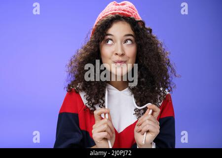 Adorable et richement mignon 20s fille avec une coiffure en forme de curly chapeau rouge chaud repliant les lèvres flirty et regardant dans le coin supérieur gauche sensuellement Banque D'Images