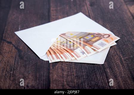 un paquet d'euros dans une enveloppe blanche ouverte sur un fond en bois sombre Banque D'Images