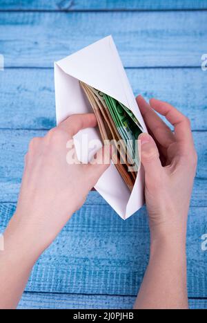 Mains tenant une enveloppe ouverte avec de l'argent sur un fond bleu Banque D'Images