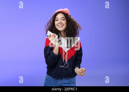 Prise de vue à la taille d'une charmante femme au poil corsé, en bonnet et en sweat-shirt pour écouter de la musique en dansant sans souci, en jouant Banque D'Images