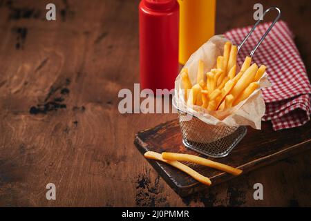 Frites dans un panier en maille de métal sur une planche de bois. Restauration rapide, cuisine américaine Banque D'Images