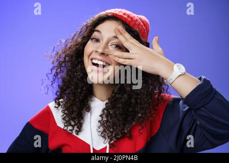 Gros plan de charismatique heureuse femme insouciante en hiver rouge beanie et sweatshirt mignon tenant les doigts près de l'oeil et peeking Banque D'Images