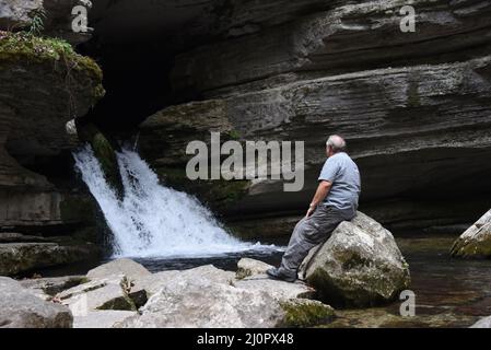 Un homme âgé est assis seul sur une grande roche en face de la chute d'eau de Blanchard Springs, près de Mountain View, Arkansas. Banque D'Images