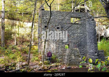 Un homme âgé, en chemise violette, se dresse à côté de l'ancien moulin de Mitchell, dans l'aire de jeux des grottes de Blanchard Springs. Il montre la comparaison de taille Banque D'Images