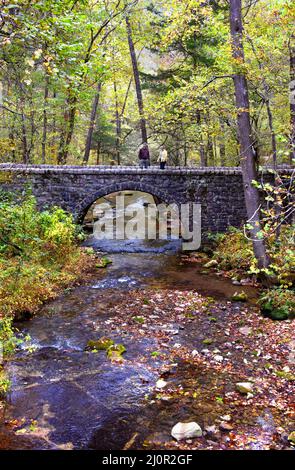 Couple traversez une demi-lune, pont en pierre au-dessus de North Sylamore Creek, Blanchard Springs Caverns, près de Mountain View, Arkansas. La saison est automne. Banque D'Images