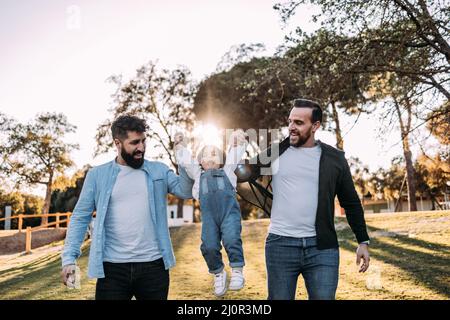 Un couple gay masculin lève leur petite fille qui rit avec joie. Concept de famille moderne et varié. Banque D'Images