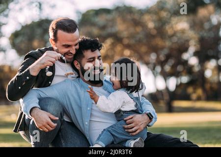 Une famille gay masculine s'embrassant et jouant avec sa petite fille dans le parc. Banque D'Images