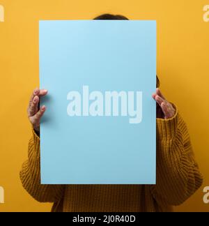 Femme dans un chandail orange tient une feuille de papier vierge sur un fond jaune. Place pour une inscription, publicité, informaa Banque D'Images