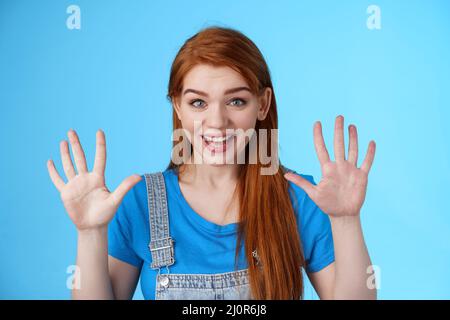 Gros plan amical joyeuse redhead fille caucasienne, long gingembre coiffure, lever les mains montrer le numéro dix, comptant lame, expliquer fin Banque D'Images