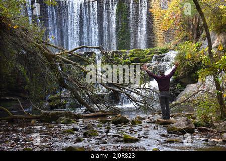 L'homme âgé se tient à la base de la chute d'eau de Mirror Lake et lève ses bras comme s'il s'y embrasse la belle région. Il a sur le pantalon gris et le shir pourpre Banque D'Images