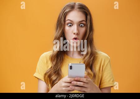 Jeune fille choqué lire des messages dans des amis smartphone lèvres pliantes des yeux dans étonnement à l'écran de téléphone portable lèvre pliante Banque D'Images