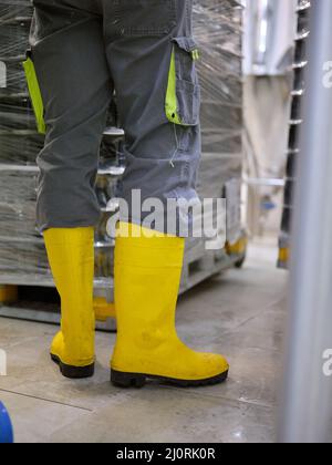 Travailleur portant des bottes de protection dans une usine artisanale de mise en conserve de bière Banque D'Images