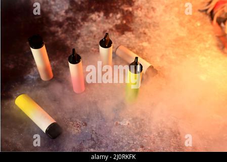 cigarettes électroniques multicolores sur fond sombre avec fumée Banque D'Images