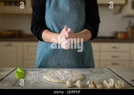 Taper les mains dans la farine d'un cuisinier dans un tablier bleu dans une cuisine maison. Banque D'Images
