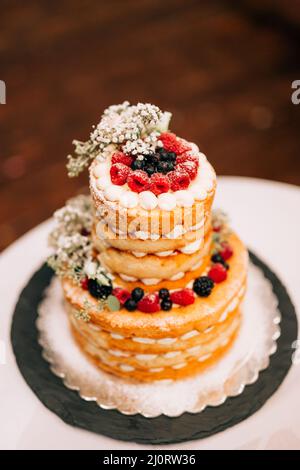 Gâteau de mariage blanc superposé décoré de baies et de fleurs sur la table Banque D'Images