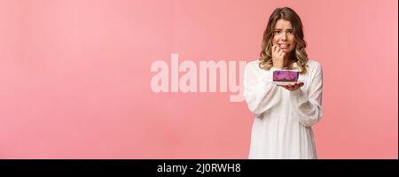 Vacances, printemps et concept de fête. Alarmée, inquiète jeune fille blonde hésitant à manger du gâteau ou non, étant sur le régime, essayer de rester en bonne santé, tenant le dessert Banque D'Images