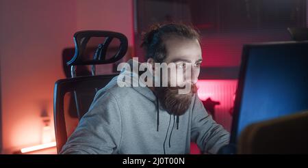 Hippie à poil long à poil long à poil long à poil long et à l'aspect jeune homme adulte jouant à des jeux sur l'ordinateur. Banque D'Images