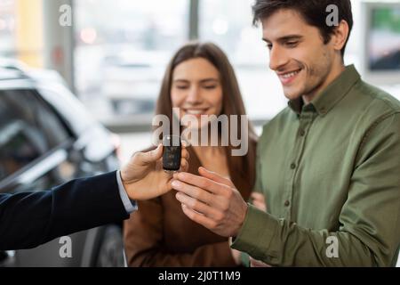 Concept d'achat ou de location d'automobiles. Un jeune couple heureux prend la clé de la voiture du vendeur d'automobiles à la concession Banque D'Images